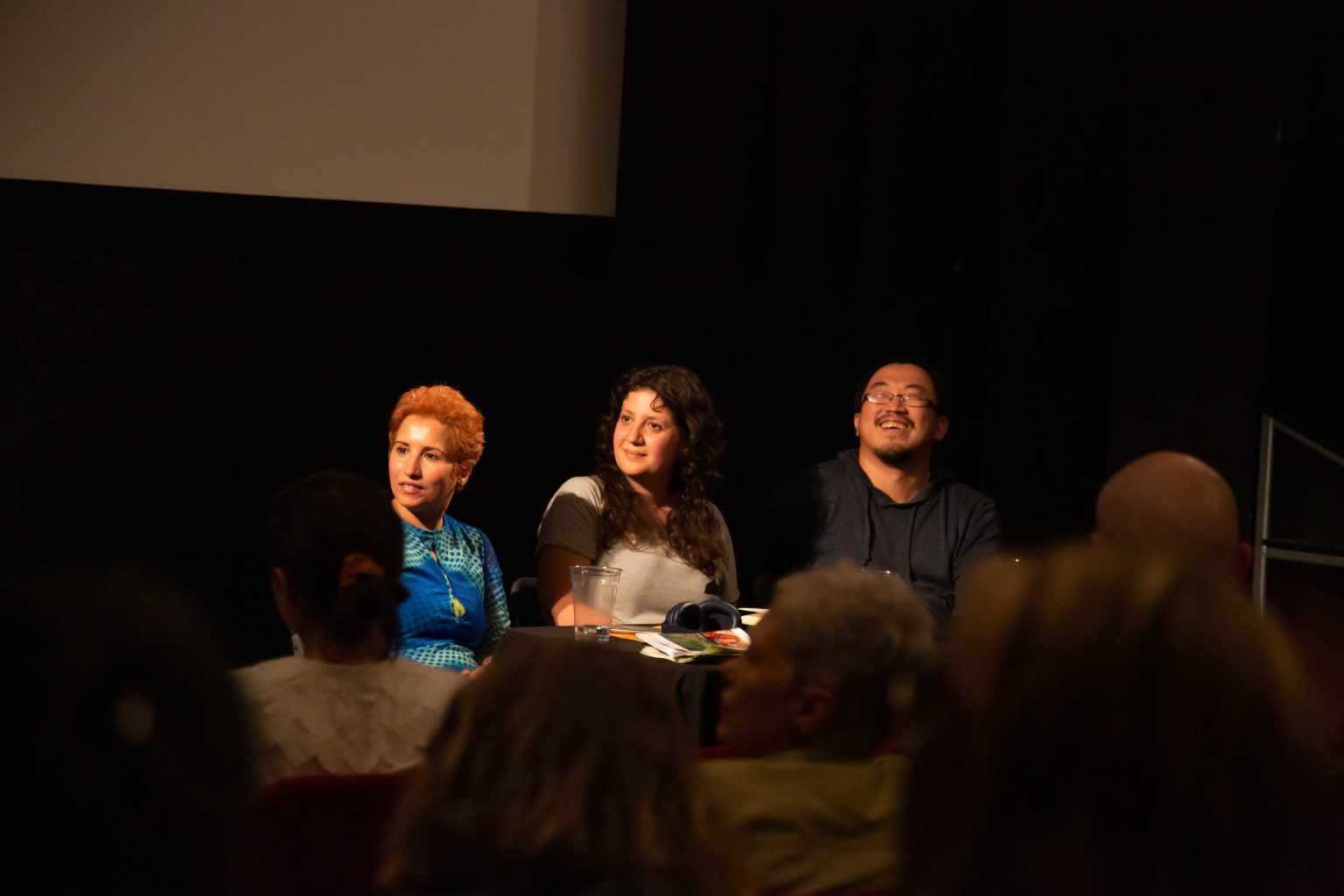 Three artists sat close together in front of an audience taking part in a panel discussion. They are all smiling and glancing to their right.