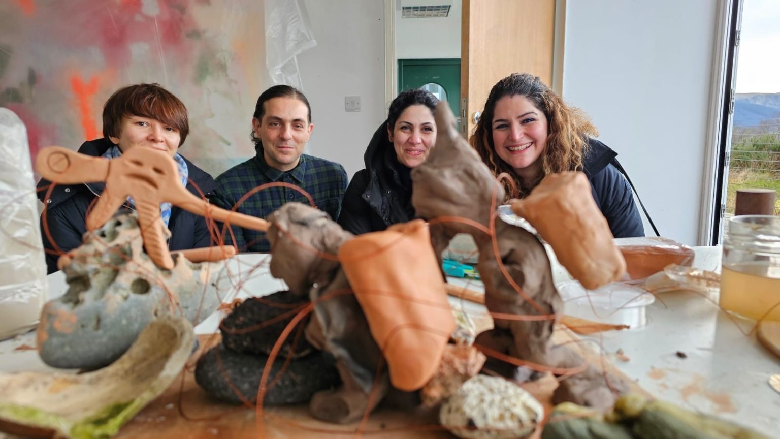 Four smiling artists crouch behind a clay and wire sculpture.