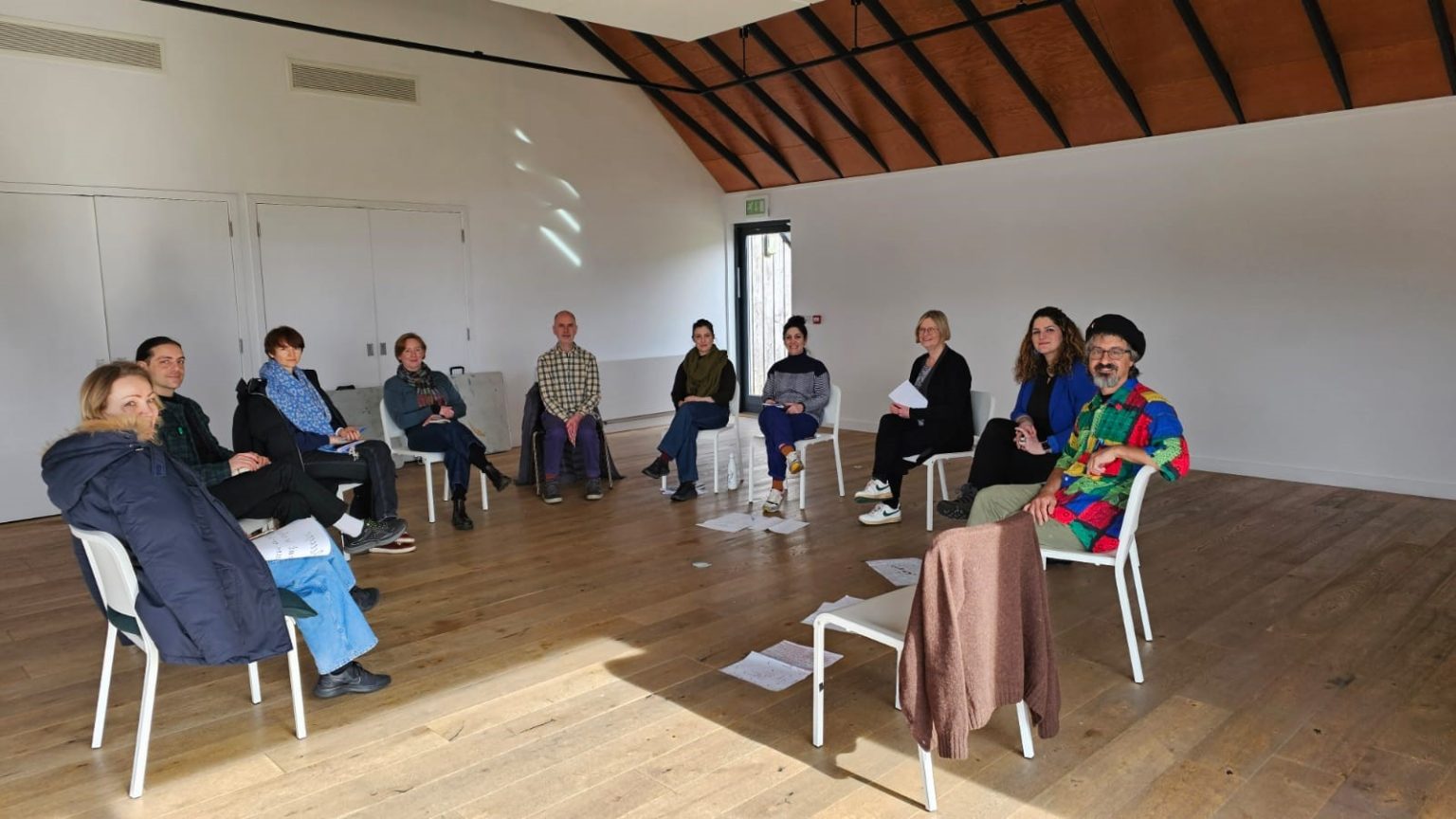 A group of artists sat together in a circle, in the middle of a bright spacious room,