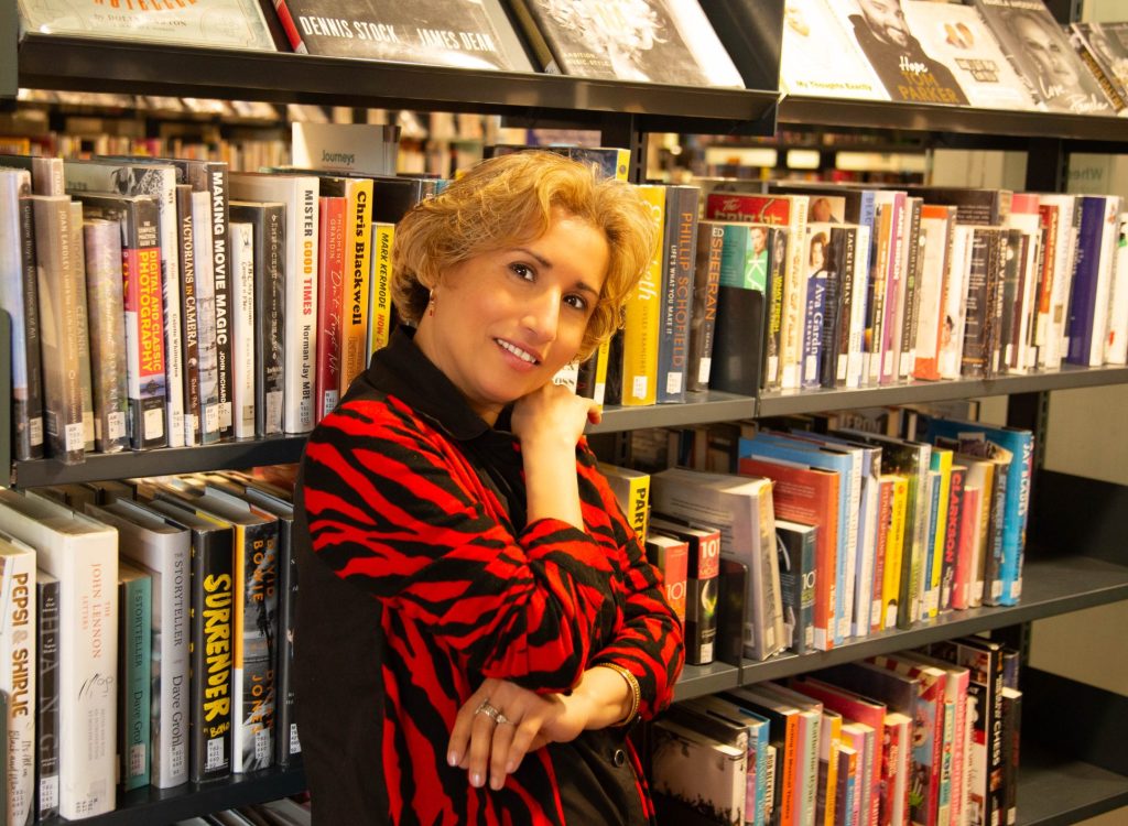 Smiling woman with blonde hair in front of a bookcase in a library